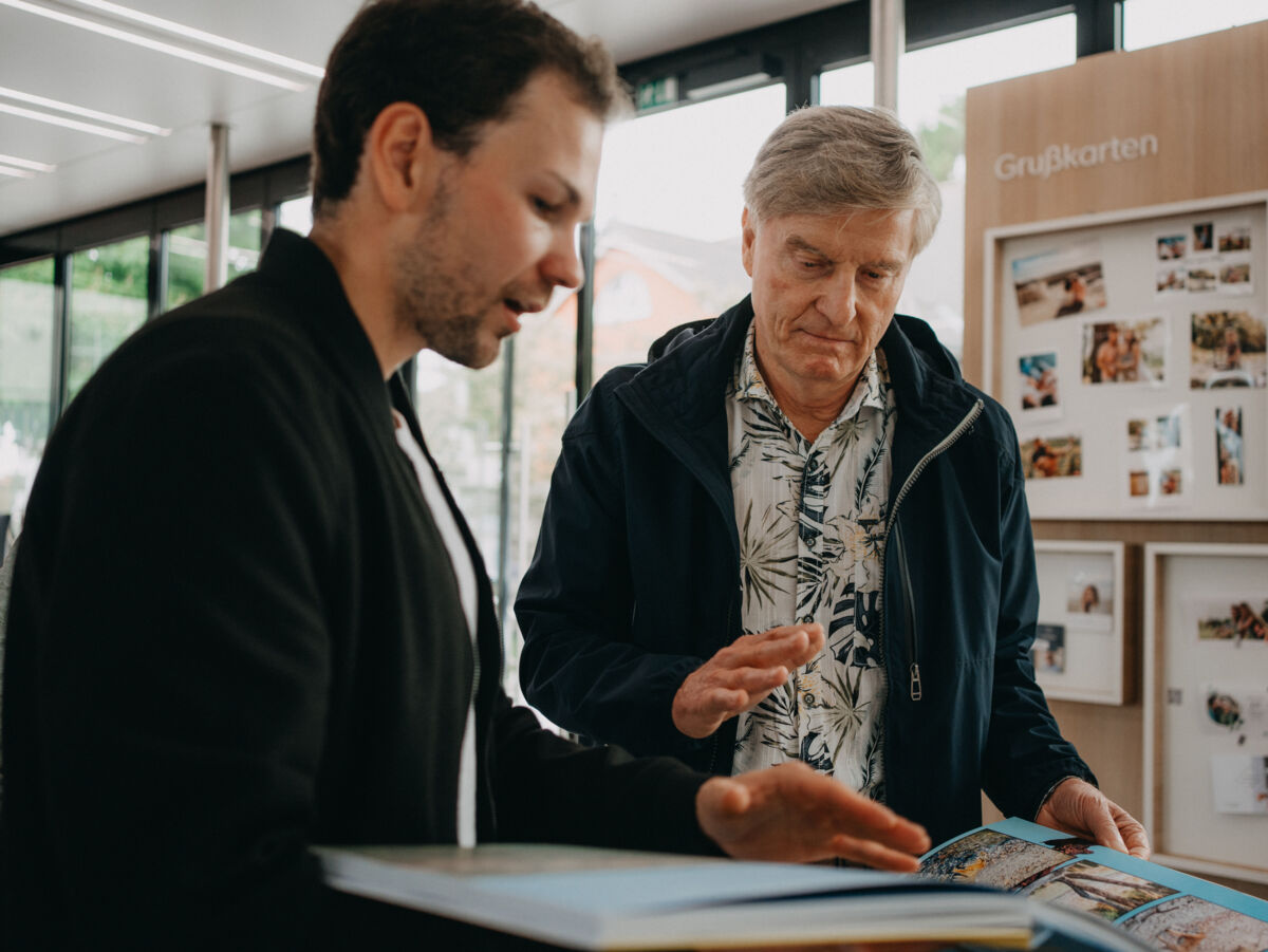 Zwei Männer betrachten interessiert ein aufgeschlagenes Fotobuch.