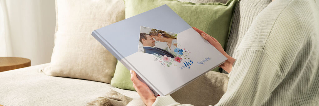 Eine Person hält ein CEWE Fotobuch mit einem schönen Cover. Die Blumenmuster und das personalisierte Design strahlen Freude und Liebe aus.