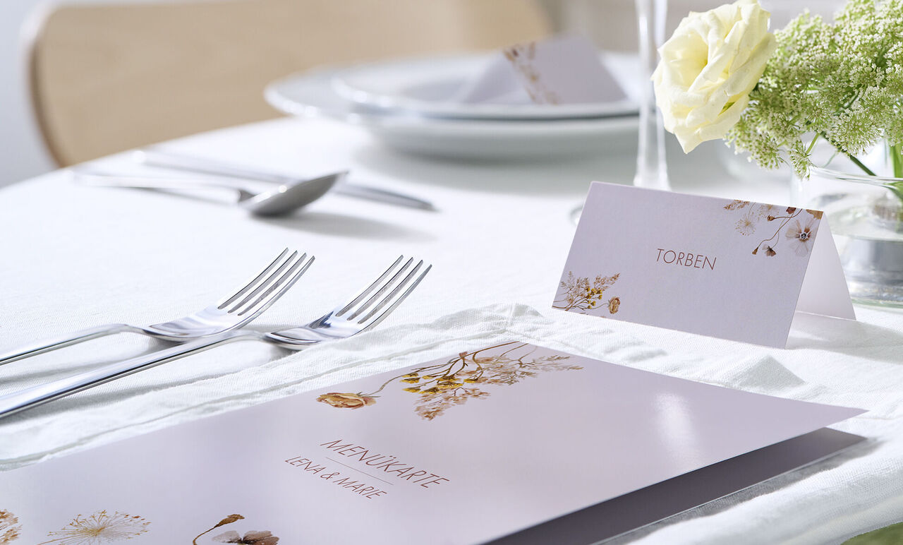 Elegante Menükarte mit floralen Details, goldenen Akzenten und passender Platzkarte auf einer stilvollen Tischdeko