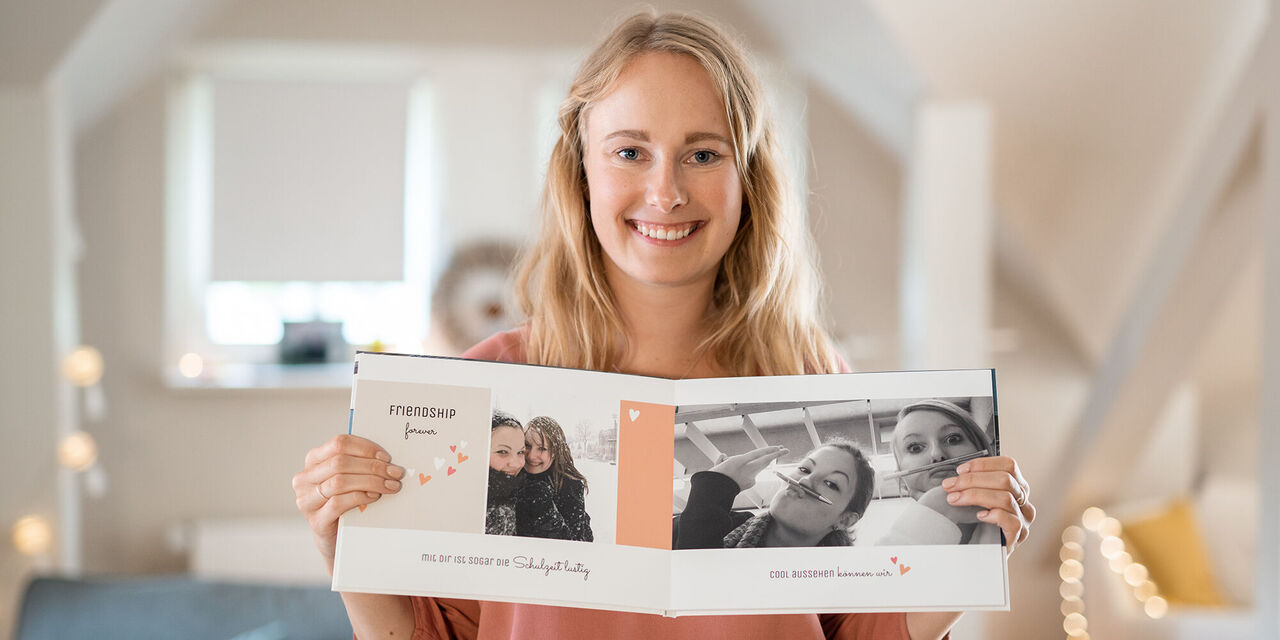 Eine Person hält ein geöffnetes Fotobuch mit Erinnerungsfotos und einem liebevollen Titel darüber in den Händen.