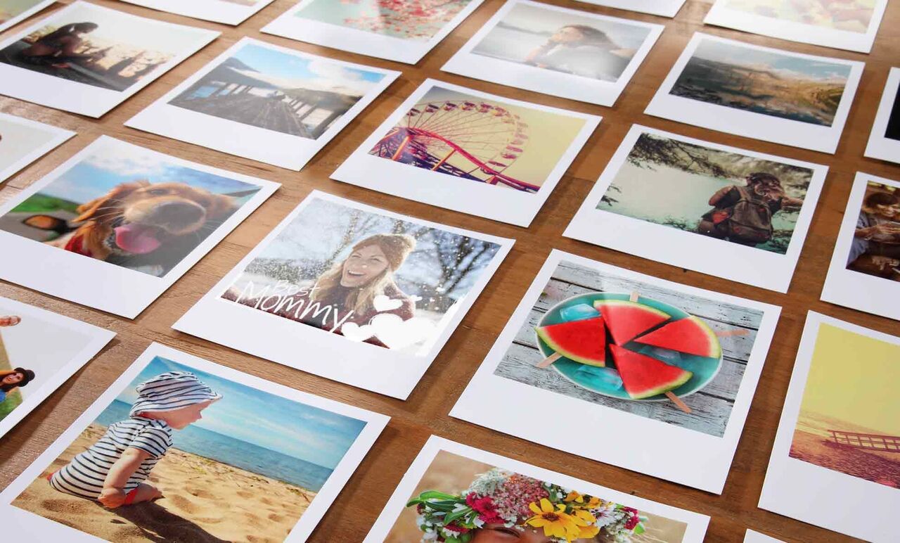 Vielfältige Fotodrucke liegen auf einem Holztisch. Die Bilder zeigen glückliche Menschen und schöne Momente wie Urlaubsreisen und bunte Früchte.