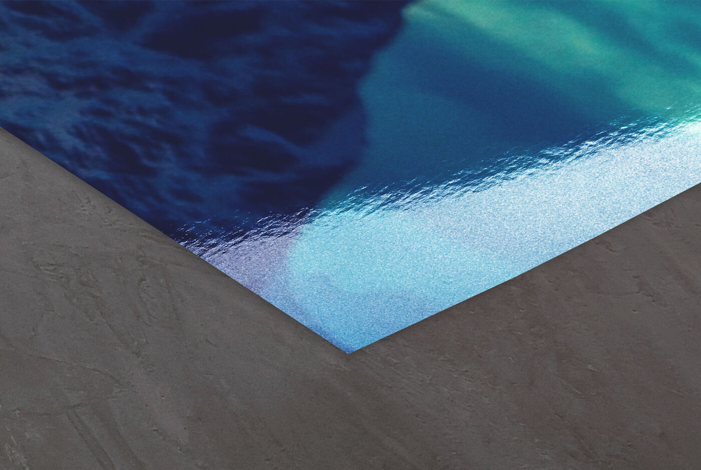 Ecke eines CEWE Posters mit glänzendem blauen Fotomotiv auf grauem Untergrund