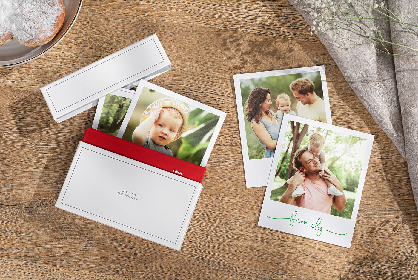 Zwei Fotos im Querformat auf einem Tisch, eines zeigt eine Familie, das andere ein Baby mit einem Erwachsenen, daneben eine dekorative Box.