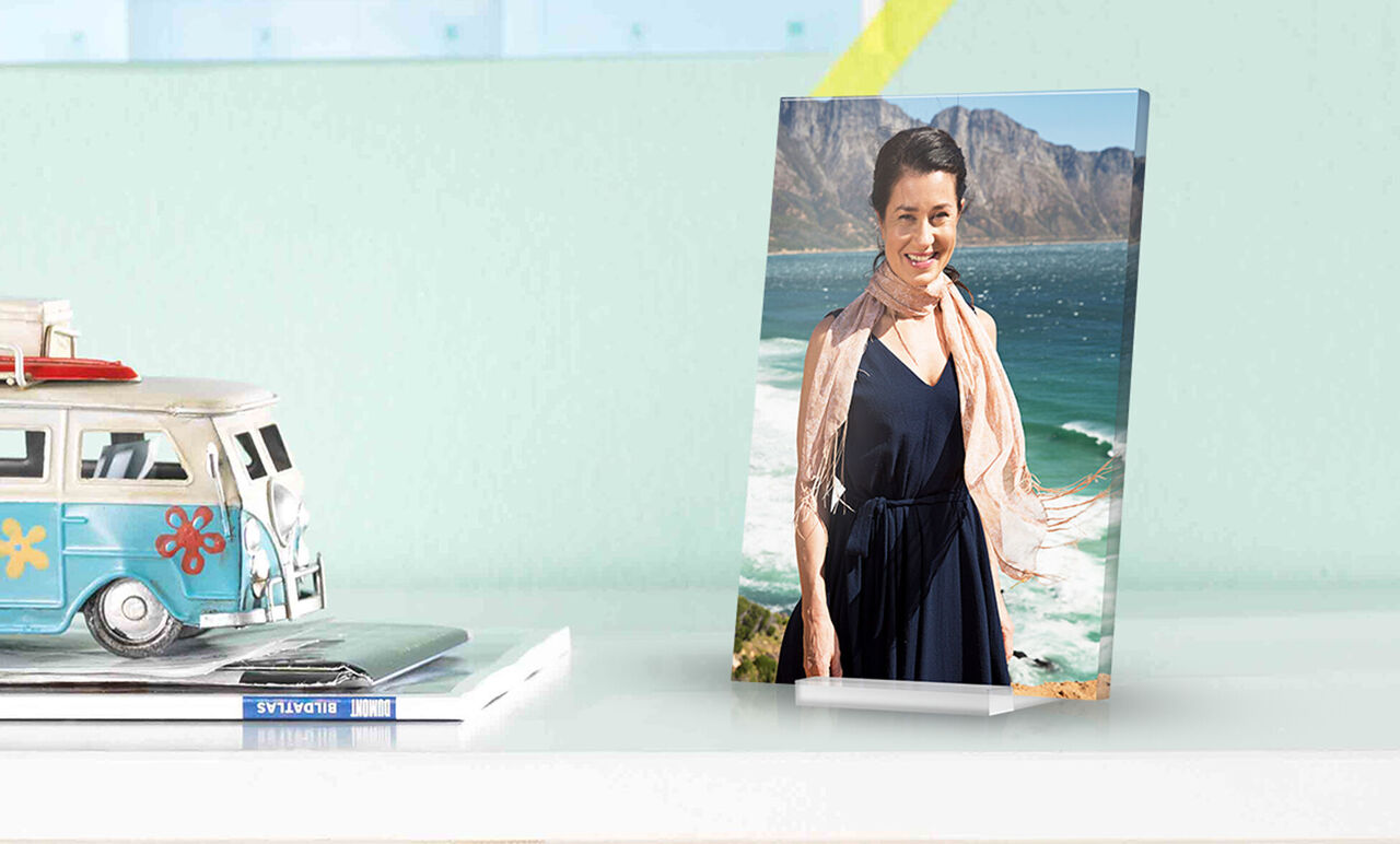 Eine Person steht am Strand mit Blick auf das Meer und die Berge im Hintergrund. Sie trägt ein elegantes Kleid und hat einen Schal um.