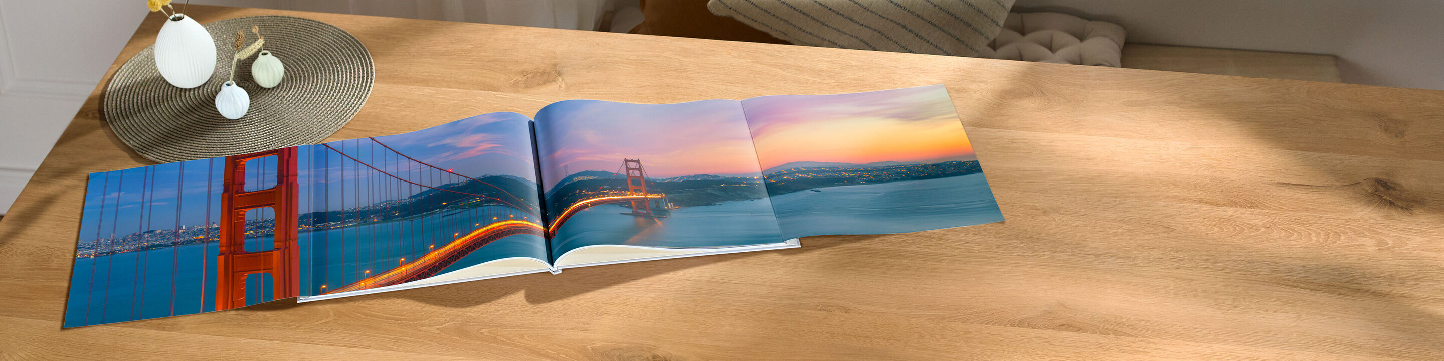 Ein offen liegendes CEWE Fotobuch mit Fotos der Golden Gate Bridge bei Sonnenuntergang auf einem Holzschreibtisch.