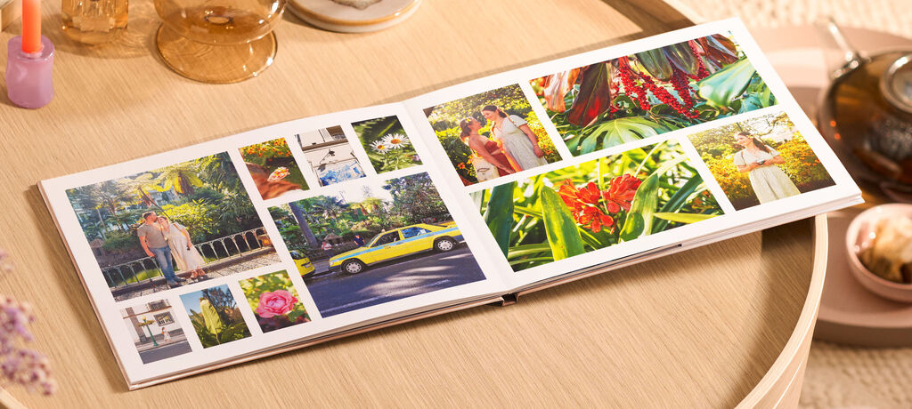 Offenes CEWE FOTOBUCH auf rundem Holztisch mit vielen bunten Reisefotos in verschiedenen Größen.