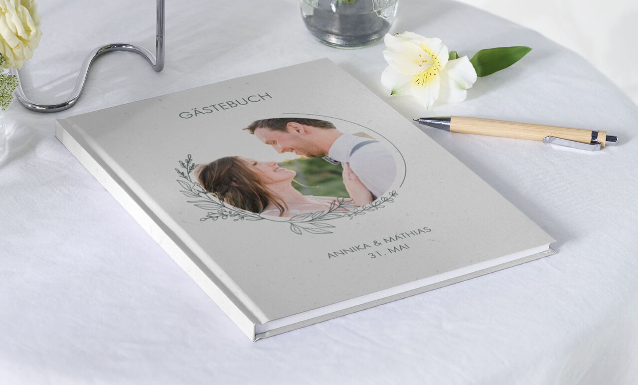 Personalisierbares Gästealbum mit romantischem Foto von einem Paar, dekoriert mit Blüten und einem Stift daneben