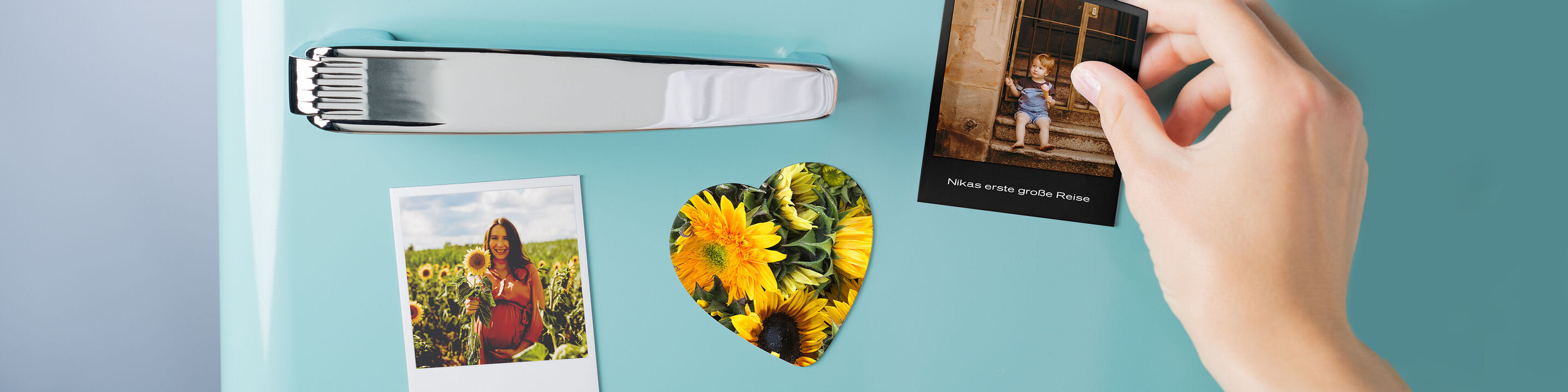 Eine Hand hängt ein Bild und ein herzförmiges Foto aus Sonnenblumen an einem Kühlschrank.