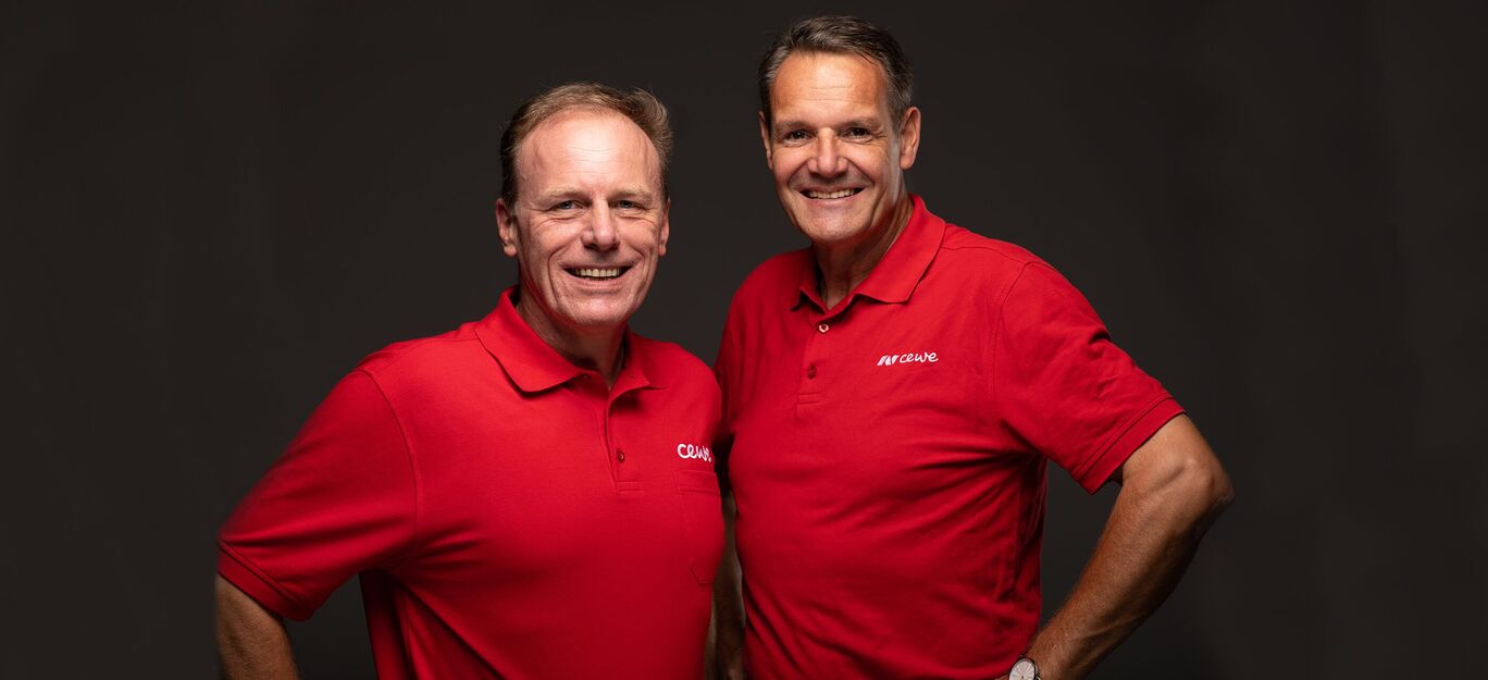 Zwei Männer in roten Poloshirts posieren freundlich.