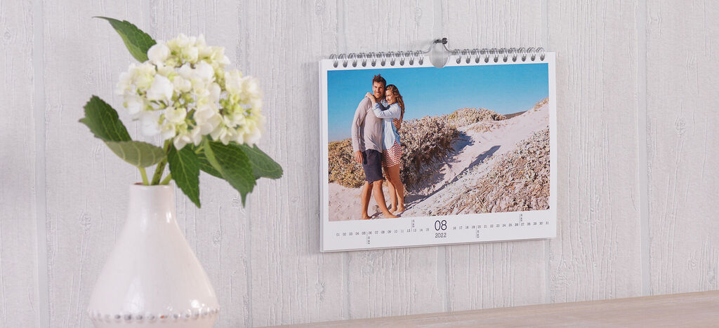 Kalender mit einem Paar am Strand, blühende Blumen im Hintergrund.