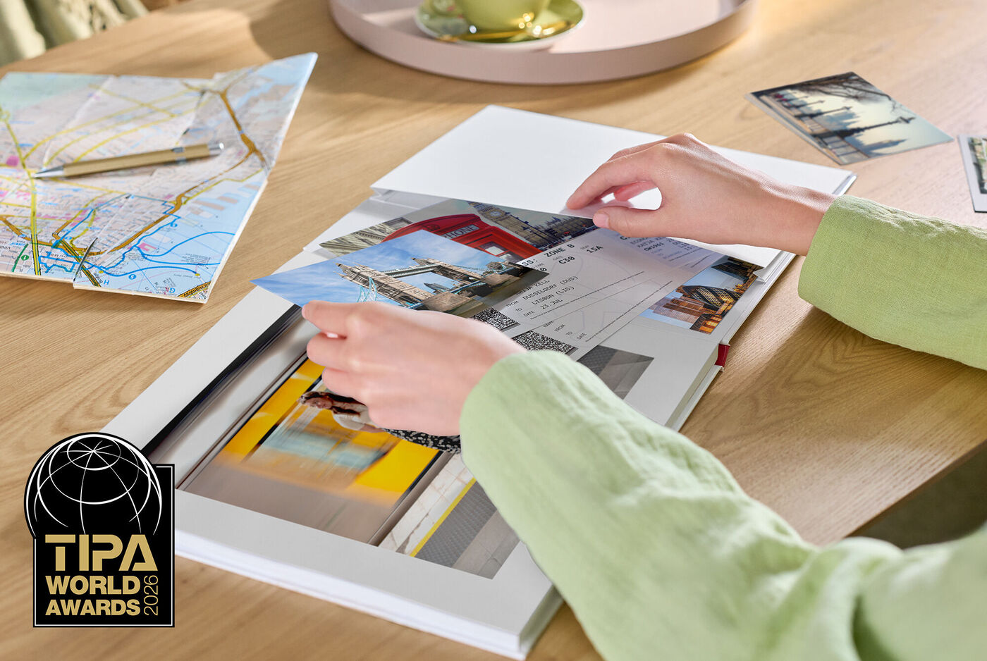 Hände ordnen Fotos in ein CEWE FOTOBUCH, auf dem Tisch liegen weitere Bilder und eine Landkarte