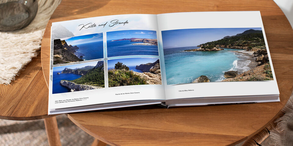 Ein geöffnetes Fotobuch zeigt wunderschöne Strandlandschaften. Die Seiten sind mit Bildern von Stränden und Klippen gefüllt. Der Tisch, auf dem das Buch liegt, ist aus Holz.