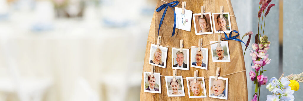 Eine holzfarbene Wand mit vielen Fotos, die mit Wäscheklammern befestigt sind. Die Fotos zeigen fröhliche Momente.
