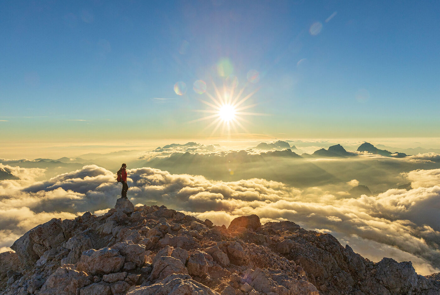 Eine Person steht auf einem Berggipfel und genießt den Sonnenaufgang über den Wolken