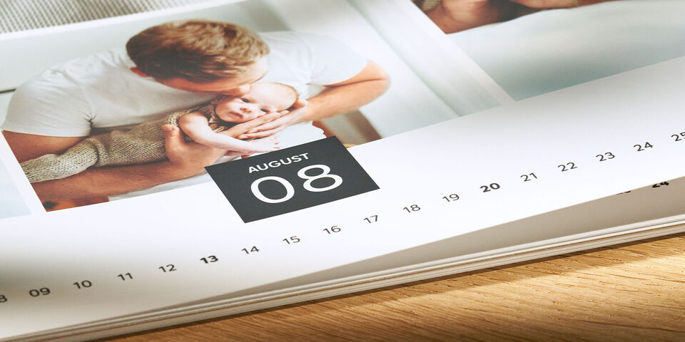 Ein offener Fotokalender zeigt einen süßen Moment zwischen einem Vater und seinem Baby im Monat August.