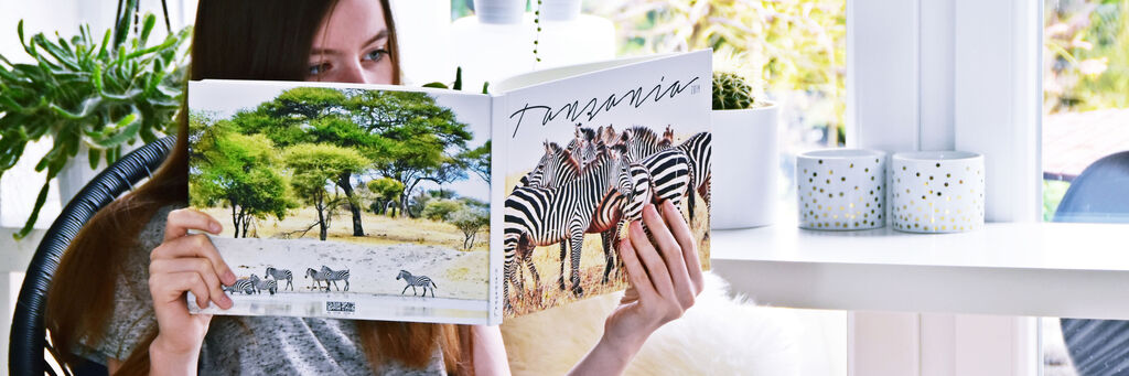 Eine Person blättert durch ein CEWE Fotobuch über Tansania mit Bildern von Zebras und afrikanischer Landschaft.