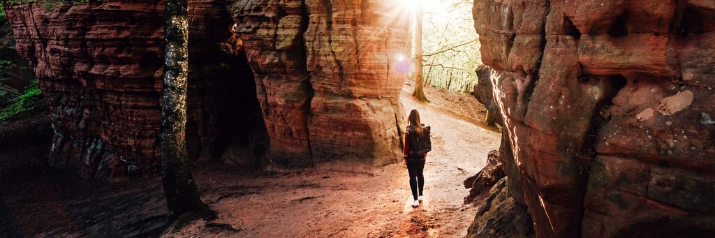 Eine Person geht einen Weg durch eine wunderschöne, sonnendurchflutete Schlucht. Die Farben des Felsens strahlen warm.