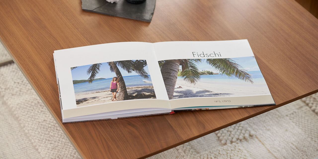 Ein offenes Fotobuch zeigt eine Strandlandschaft auf Fidschi mit Palmen und zwei Personen.