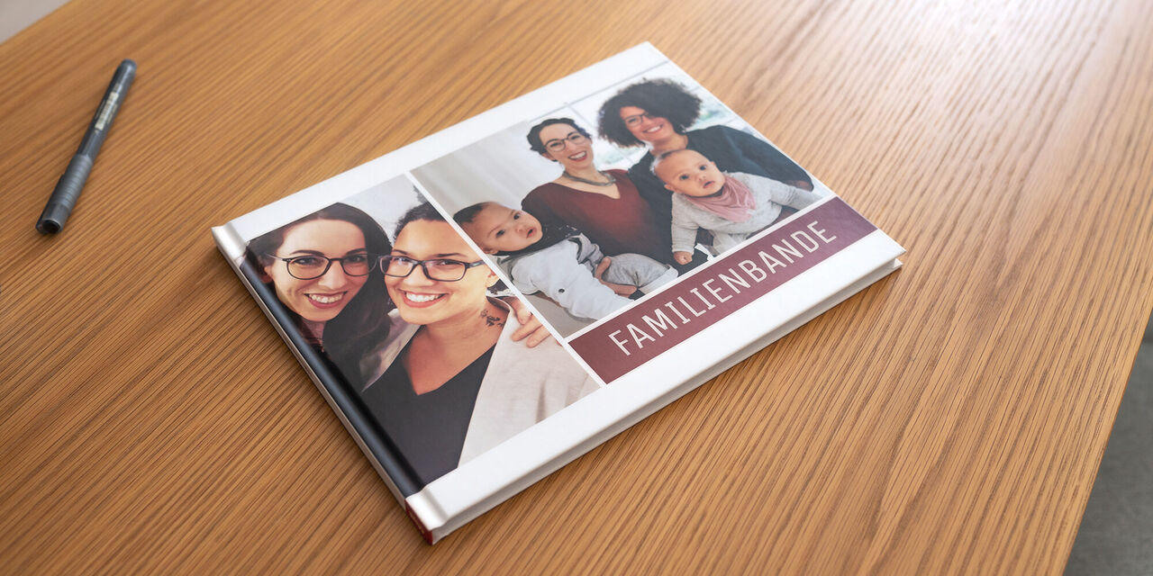 Ein CEWE FOTOBUCH mit dem Titel 'Familienbande' auf einem Holztisch, umgeben von einem Stift und fröhlichen Erinnerungen
