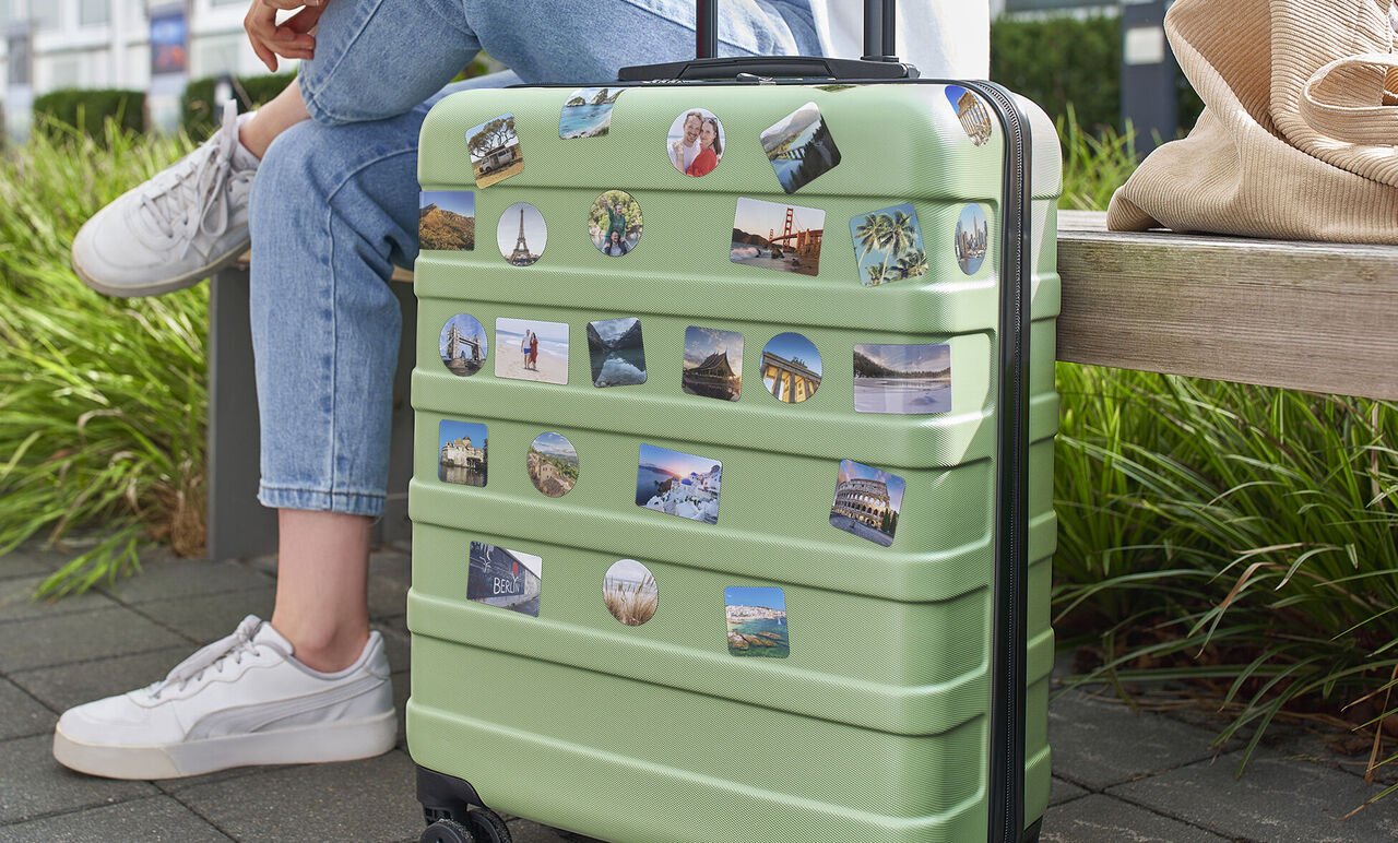 Grüne Reisetasche mit Erinnerungsstickern auf einer Bank.