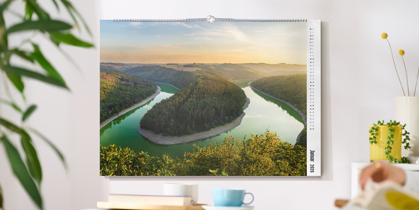 CEWE Fotokalender an Wand mit Flussbiegung, grünen Hügeln und weiter Landschaft