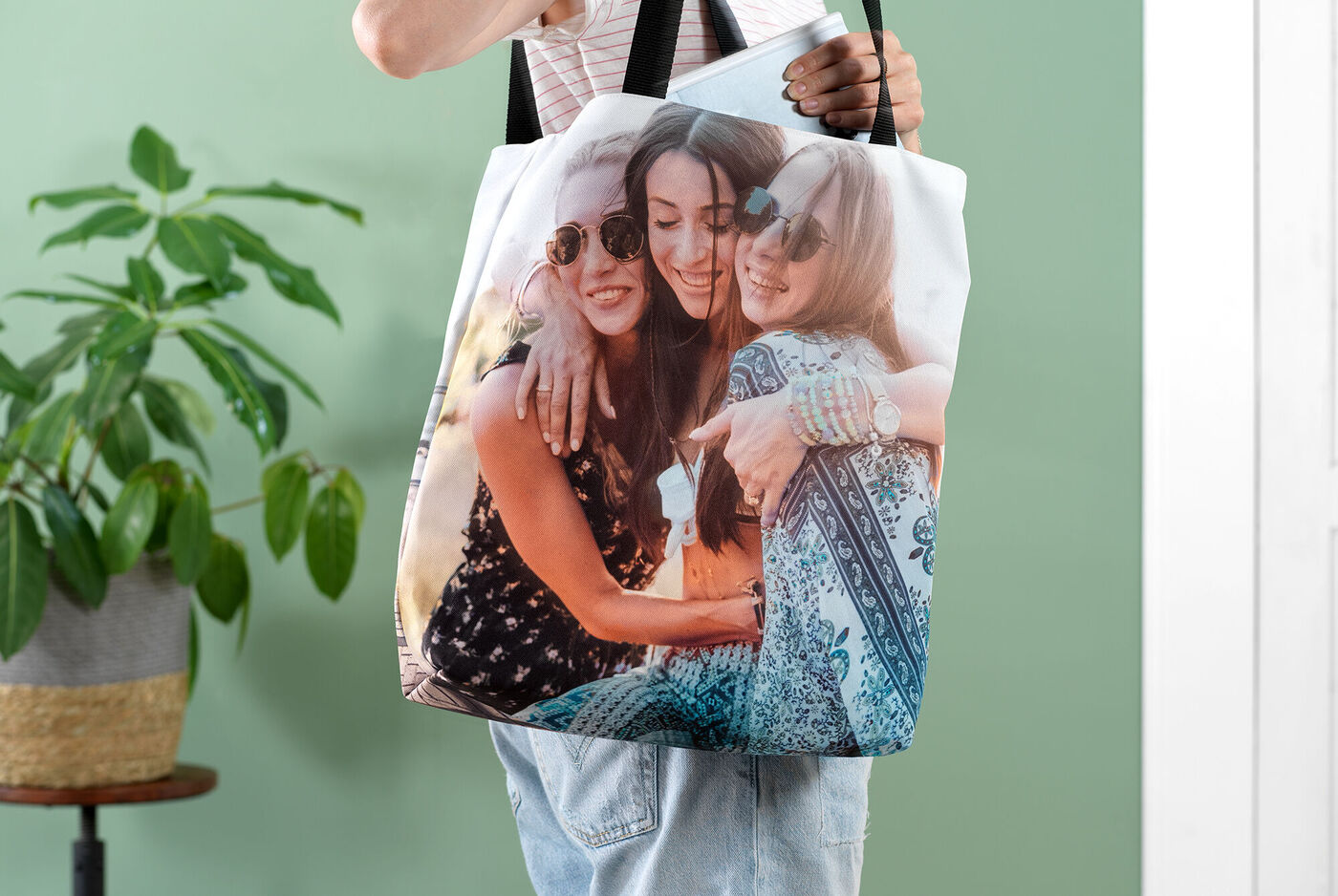 Person hält eine süße Tasche mit einem Fotodruck von Freunden. Die Tasche zeigt einen herzlichen Moment zwischen zwei Menschen, umgeben von einer freundlichen Atmosphäre.
