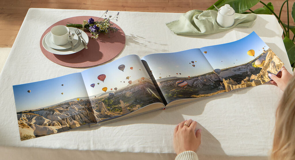 Eine Person blättert in einem offenen Fotobuch mit Luftballons und Landschaften im Hintergrund