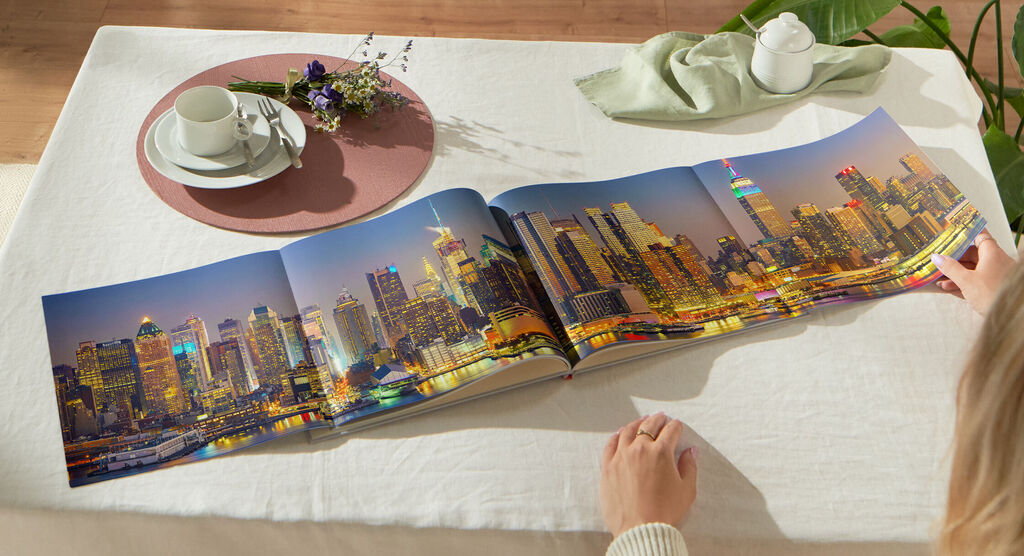 Eine Person blättert durch ein geöffnetes Fotobuch mit einer Stadtansicht von Philadelphia bei Nacht auf einem Tisch.