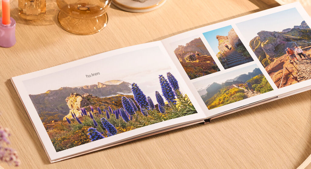 CEWE FOTOBUCH mit bunten Naturfotos von Bergen und Blumen auf einem Holztisch