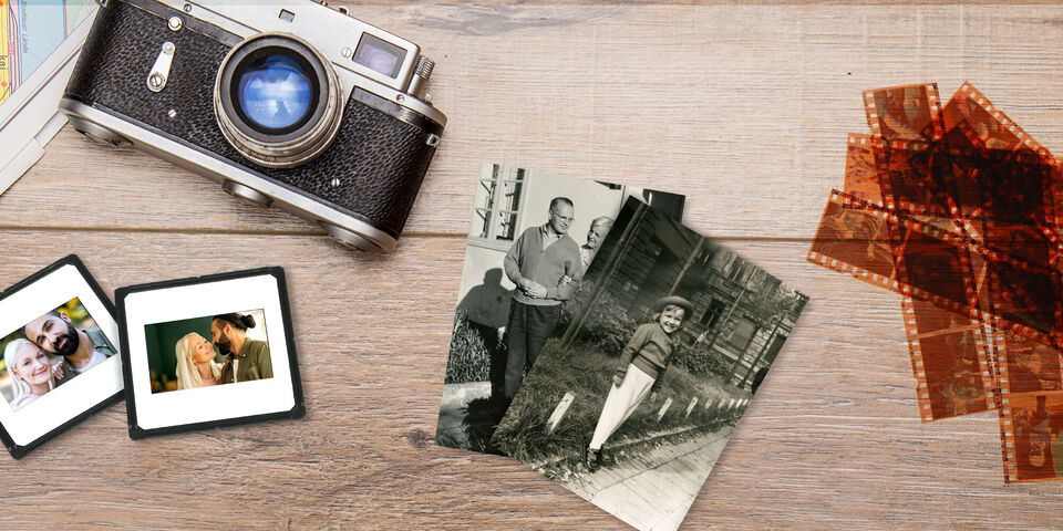 Eine alte Kamera auf einem Holztisch, umgeben von Familienfotos in Rahmen und Filmnegativen, die Erinnerungen bewahren
