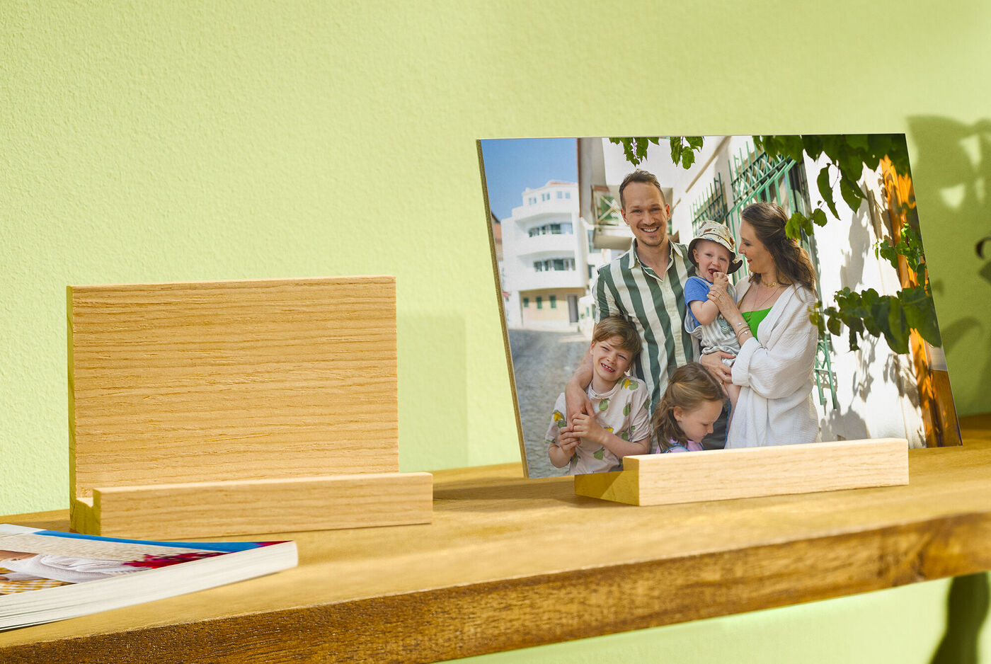 Familie posiert glücklich vor einem Haus, mit einem kleinen Fotobuch auf dem Tisch
