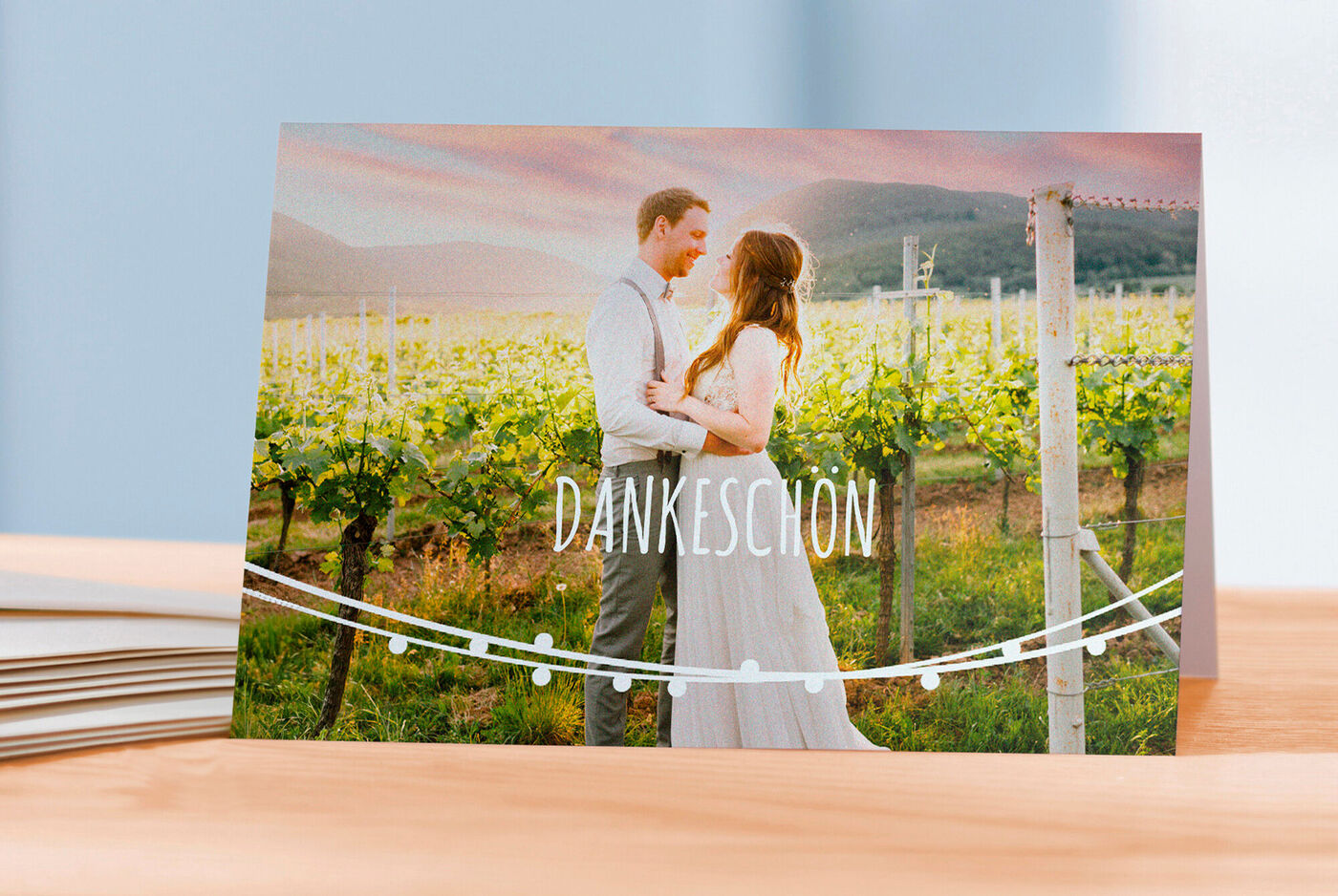 Ein Paar steht in einem Weinberg und hält sich an den Händen. Sie feiern mit einer Dankeskarten zur Hochzeit.