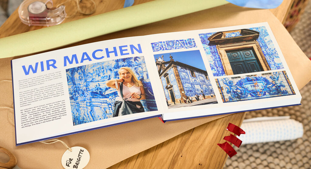 Offenes CEWE FOTOBUCH mit blauen Fliesenmotiven und Reisebildern auf einem Holztisch.