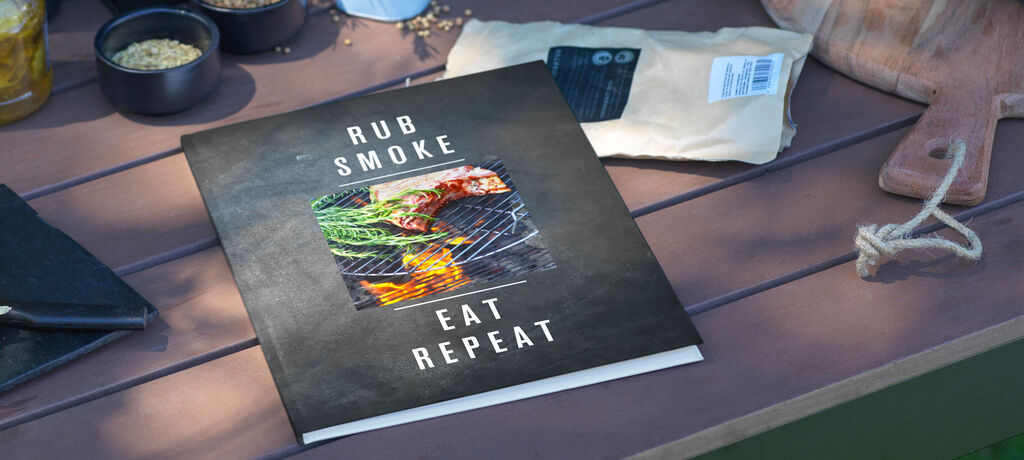 Ein geschmackvoll gestaltetes Kochbuch mit dem Titel "Rub Smoke Eat Repeat" auf einem Tisch mit verschiedenen Zutaten.
